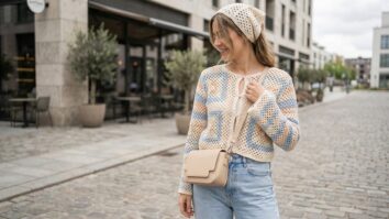 Mulher sorrindo usando blusa e bandana de croche em tons leves de verao em ambiente urbano contemporaneo com luz natural