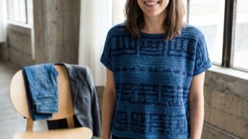 Mulher sorrindo usando blusa de croche azul artesanal em ambiente interno minimalista com luz natural