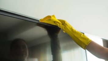 Pessoa limpando a tv na sala usando luvas amarelas
