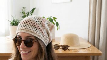 Quarto iluminado com mulher usando bandana de crochê artesanal em tons suaves ao lado de óculos de sol e chapéu de palha