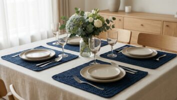 Mesa de jantar elegante com jogos americanos de croche artesanal em azul escuro, pratos de ceramica neutra, copos de vidro e arranjo floral ao centro