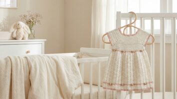 Quarto infantil delicado com vestido de croche artesanal off-white com detalhes rosa em cabide proximo a berco decorado