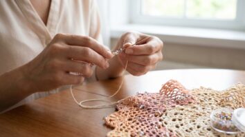 Maos aplicando micangas delicadas diretamente no fio antes de crocheta-lo, demonstrando tecnica profissional de acabamento luxuoso