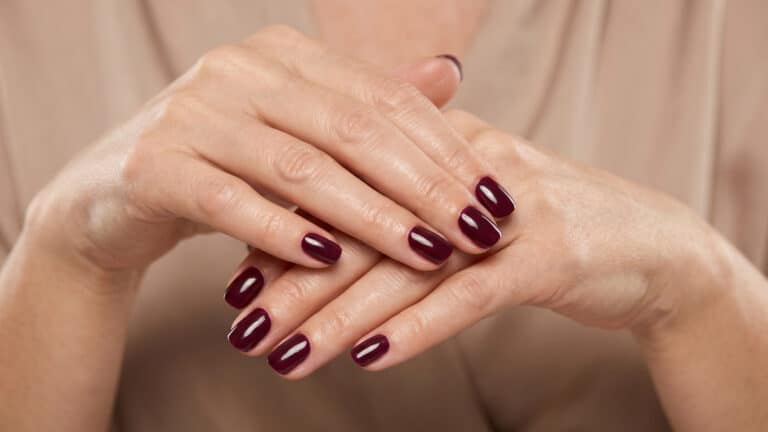 Mãos maduras com esmalte vinho elegante destacando sofisticação e cuidado.