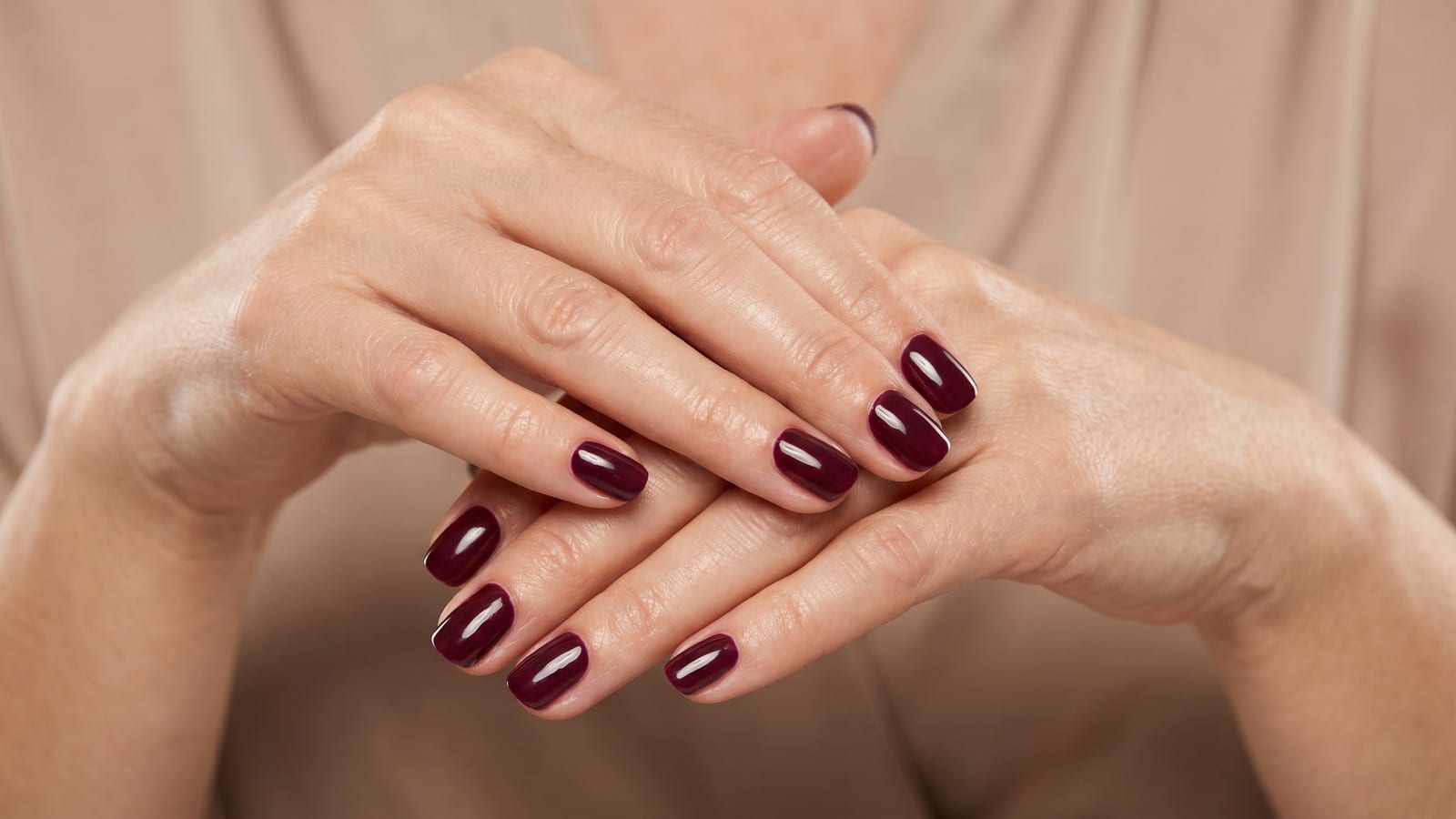 Mãos maduras com esmalte vinho elegante destacando sofisticação e cuidado.