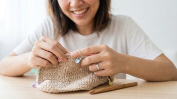 Maos de mulher usando marcadores de ponto em peca de croche, tecnica de organizacao artesanal