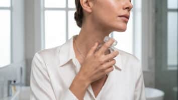 Mulher borrifando perfume no pescoço.