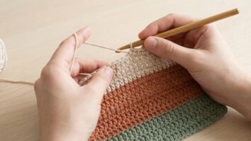 Maos trabalhando em croche com tecnica de troca de cor invisivel mostrando listras perfeitamente alinhadas