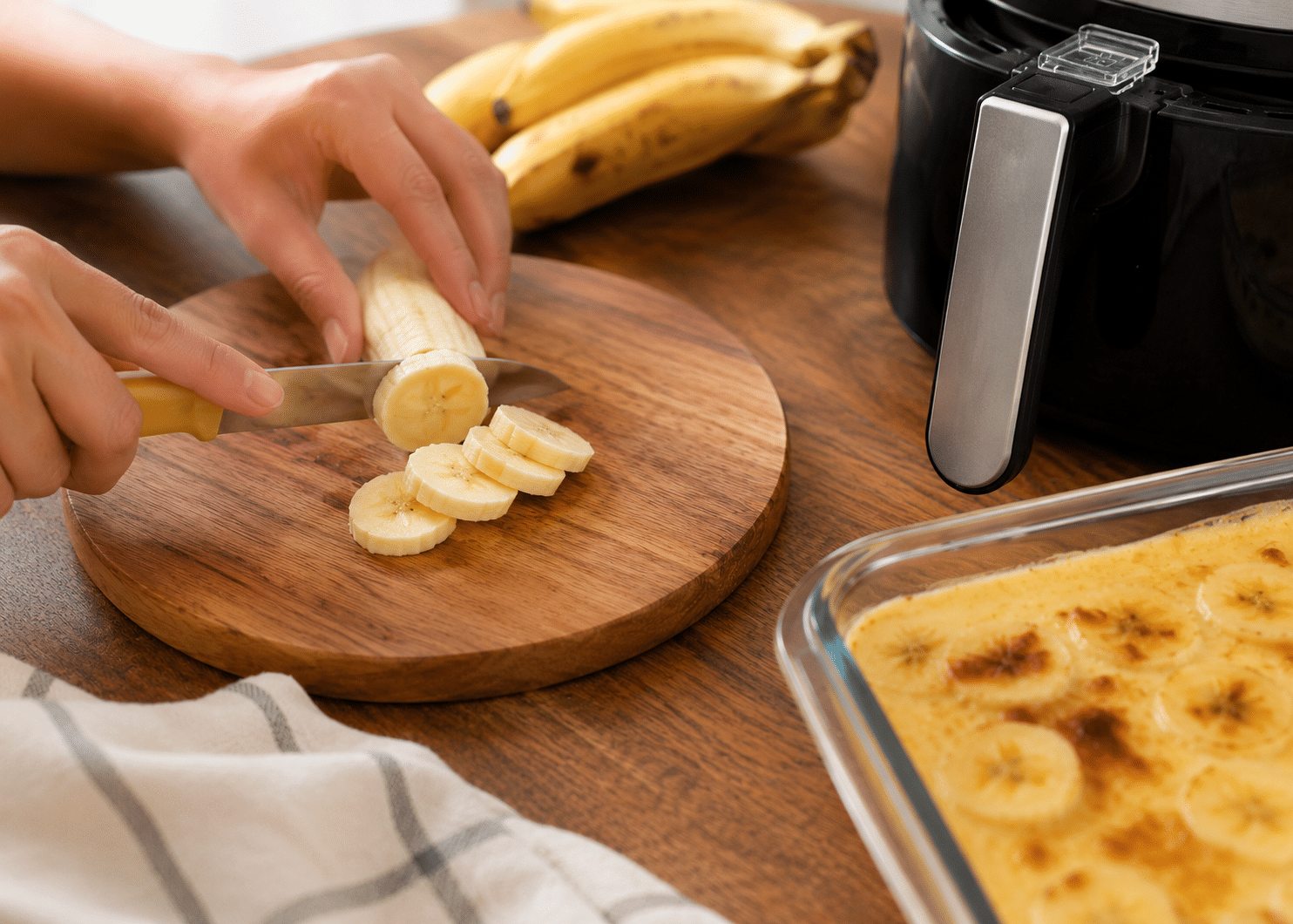 Bananas maduras sendo cortadas sobre mesa de madeira durante o preparo da banana cremosa na Air Fryer.