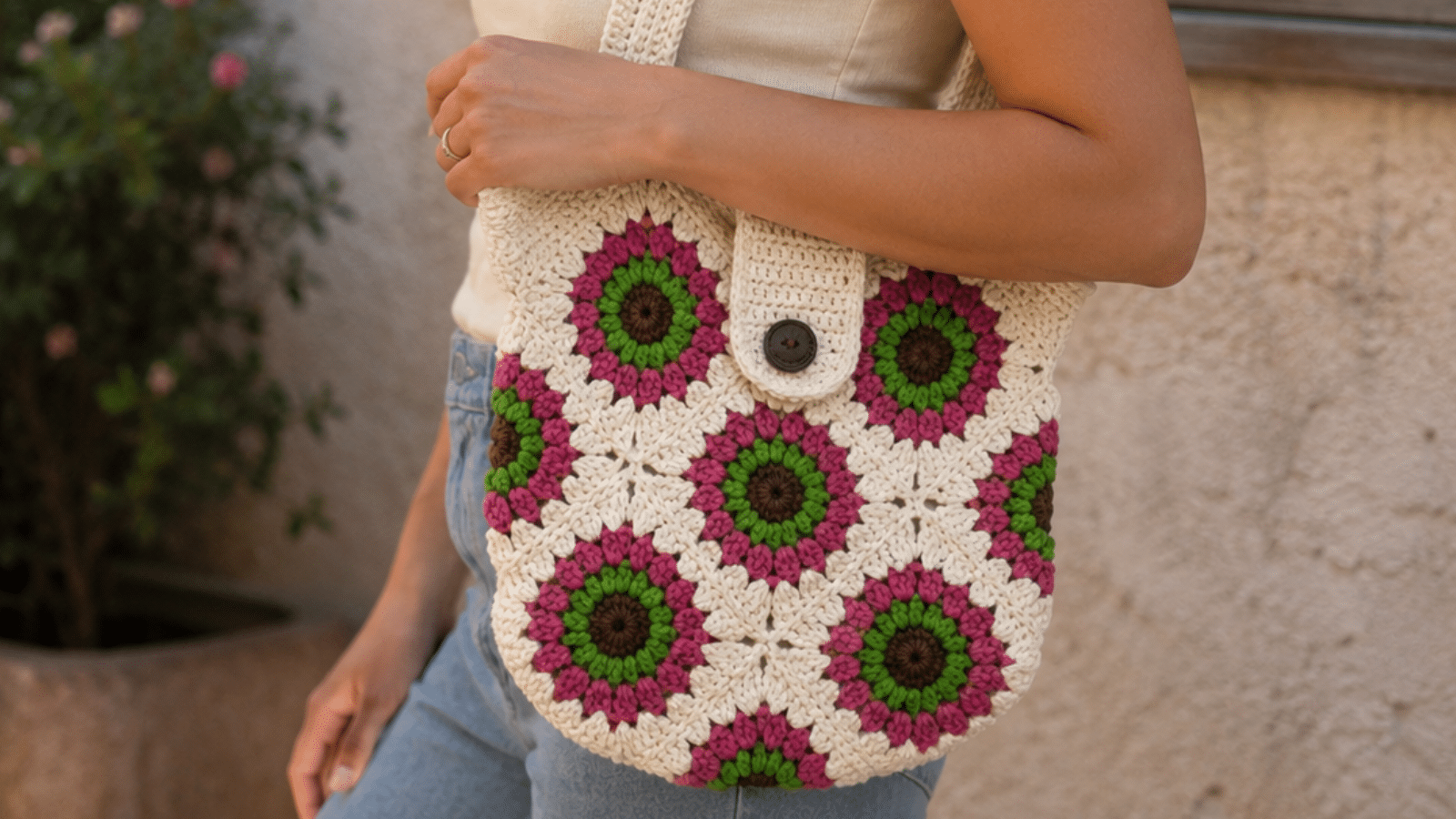 Mulher usando bolsa de crochê floral em tons de cru, rosa e verde, destacando o charme artesanal da peça feita à mão em um look casual.