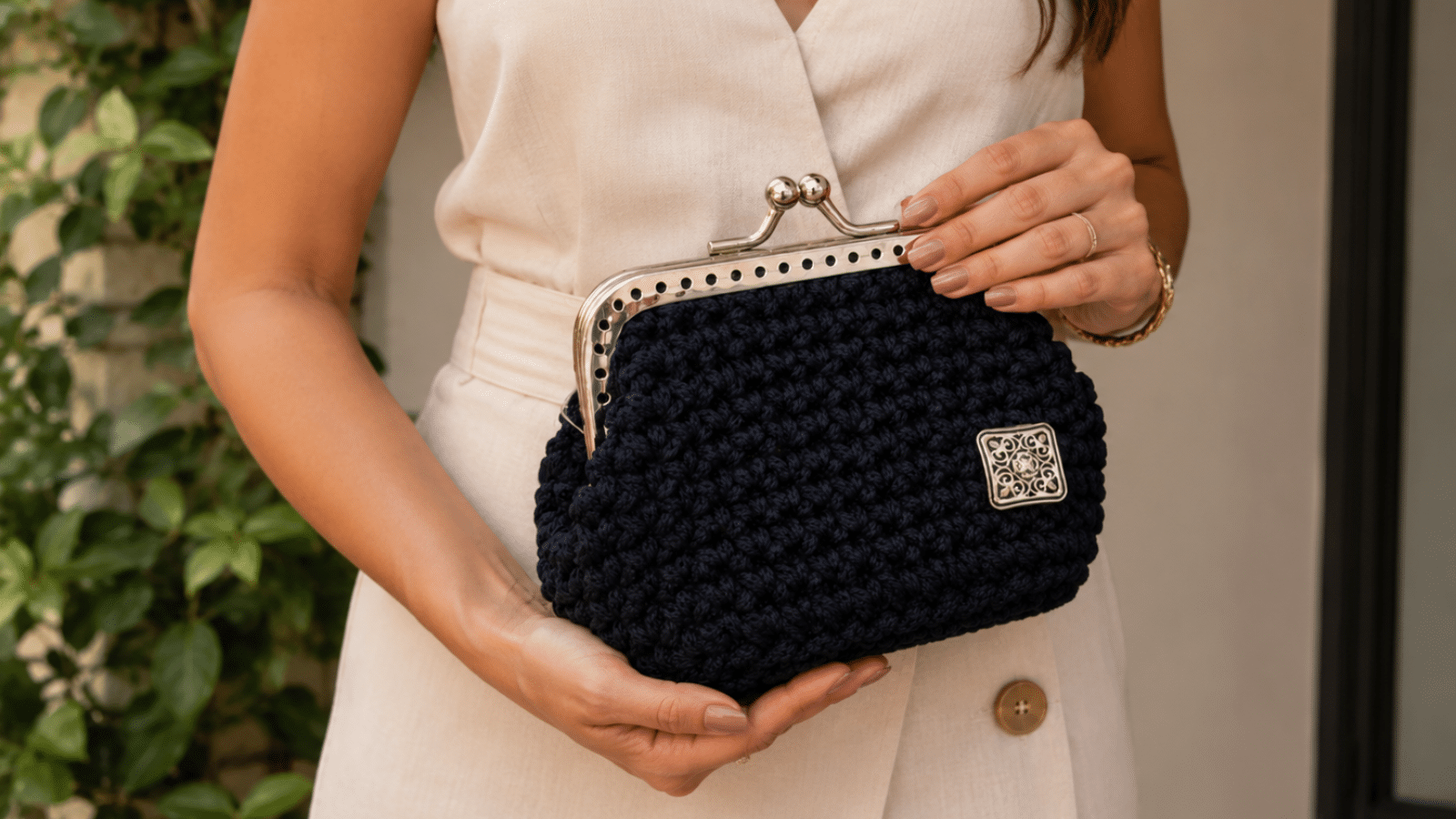 Mulher segurando bolsa de mão em crochê preto com fecho metálico, destacando a textura artesanal e o acabamento elegante da peça.