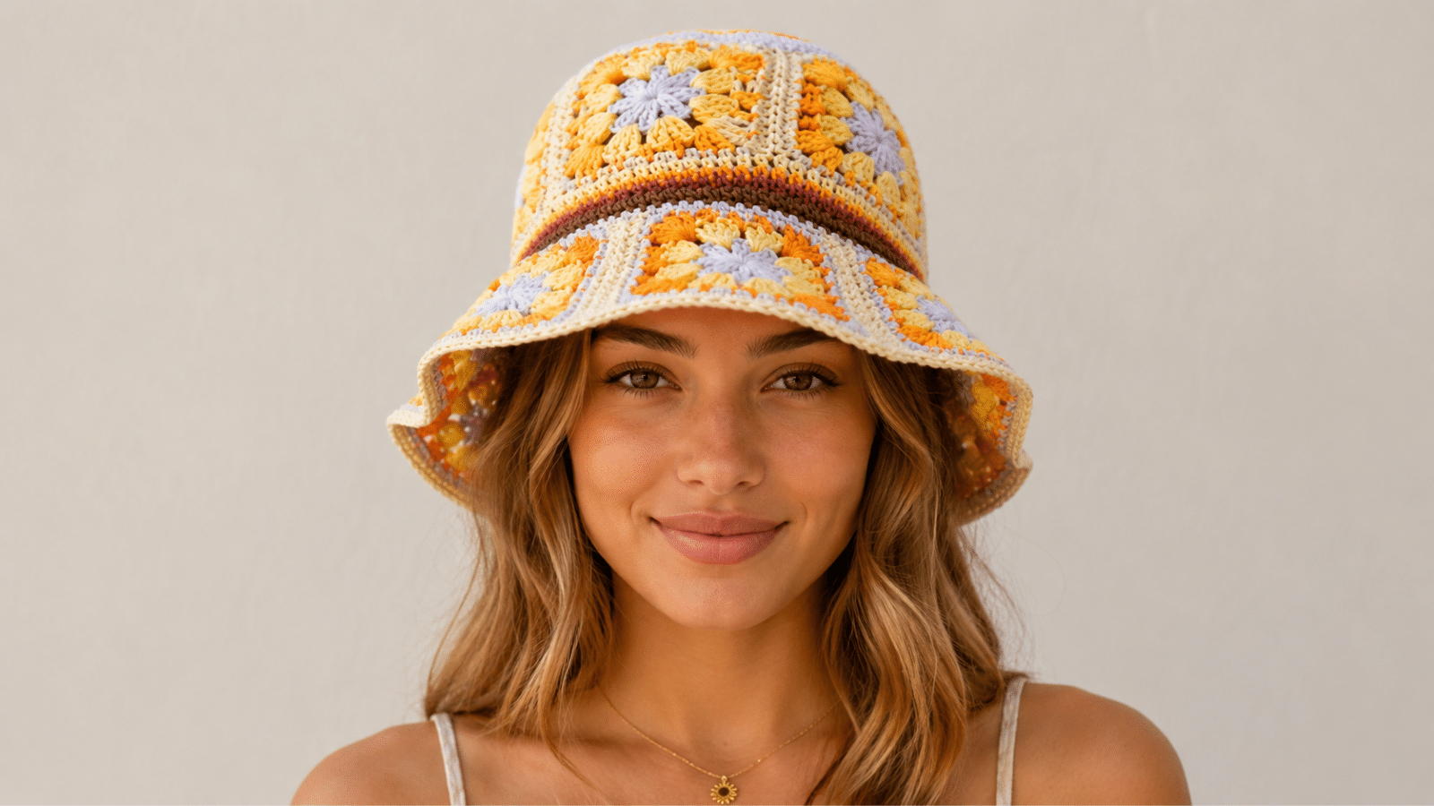 Mulher usando chapéu bucket de crochê com granny squares coloridos, em tons de amarelo, laranja e bege, com visual leve e artesanal.