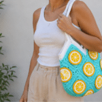 Mulher usando bolsa de crochê azul com detalhes de laranja, alça branca e estilo artesanal para looks leves de verão.
