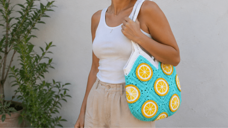 Mulher usando bolsa de crochê azul com detalhes de laranja, alça branca e estilo artesanal para looks leves de verão.