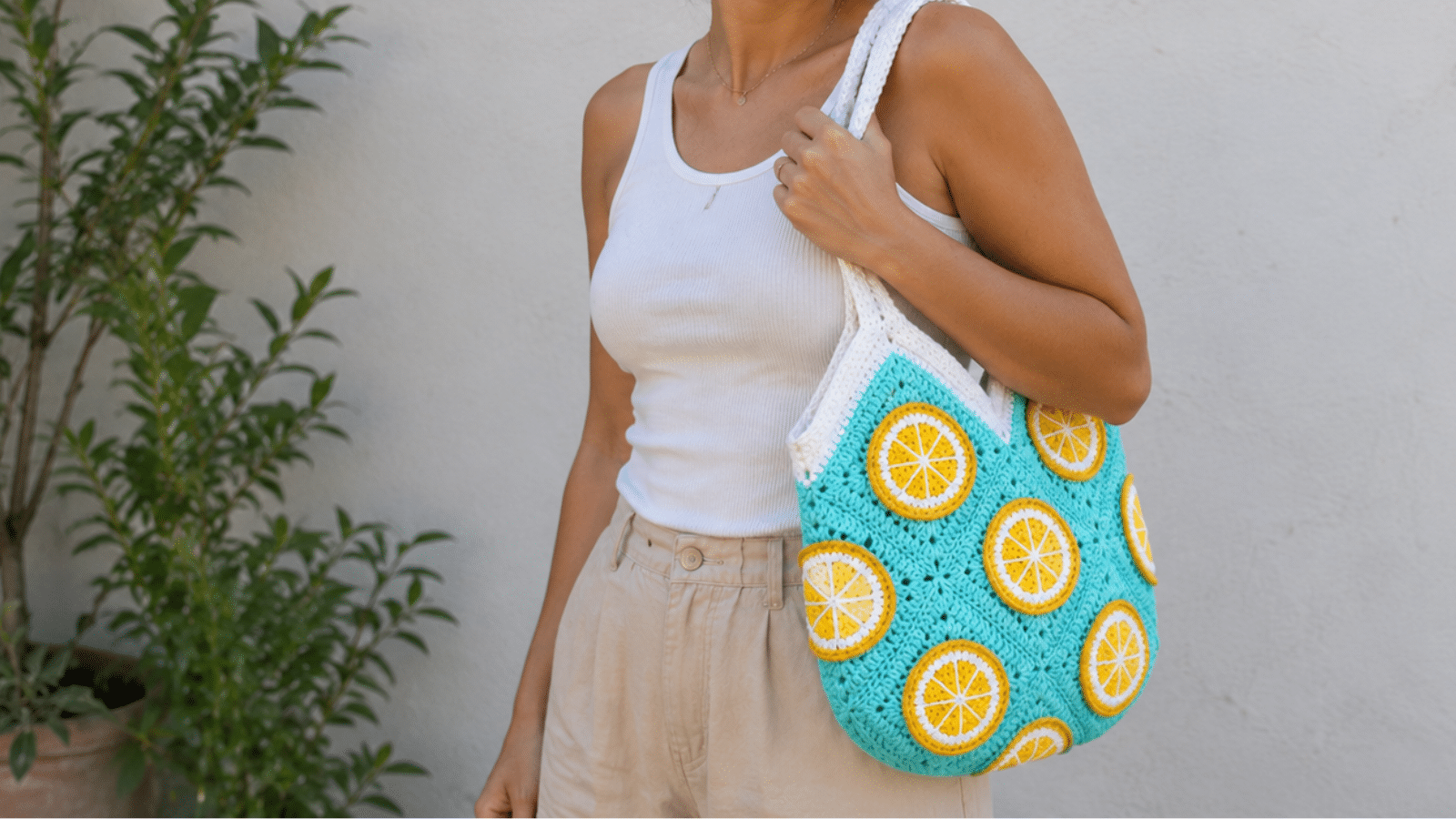 Mulher usando bolsa de crochê azul com detalhes de laranja, alça branca e estilo artesanal para looks leves de verão.