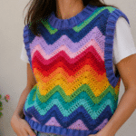 Mulher usando colete de crochê arco-íris em zigue-zague, peça artesanal colorida para transformar looks simples.