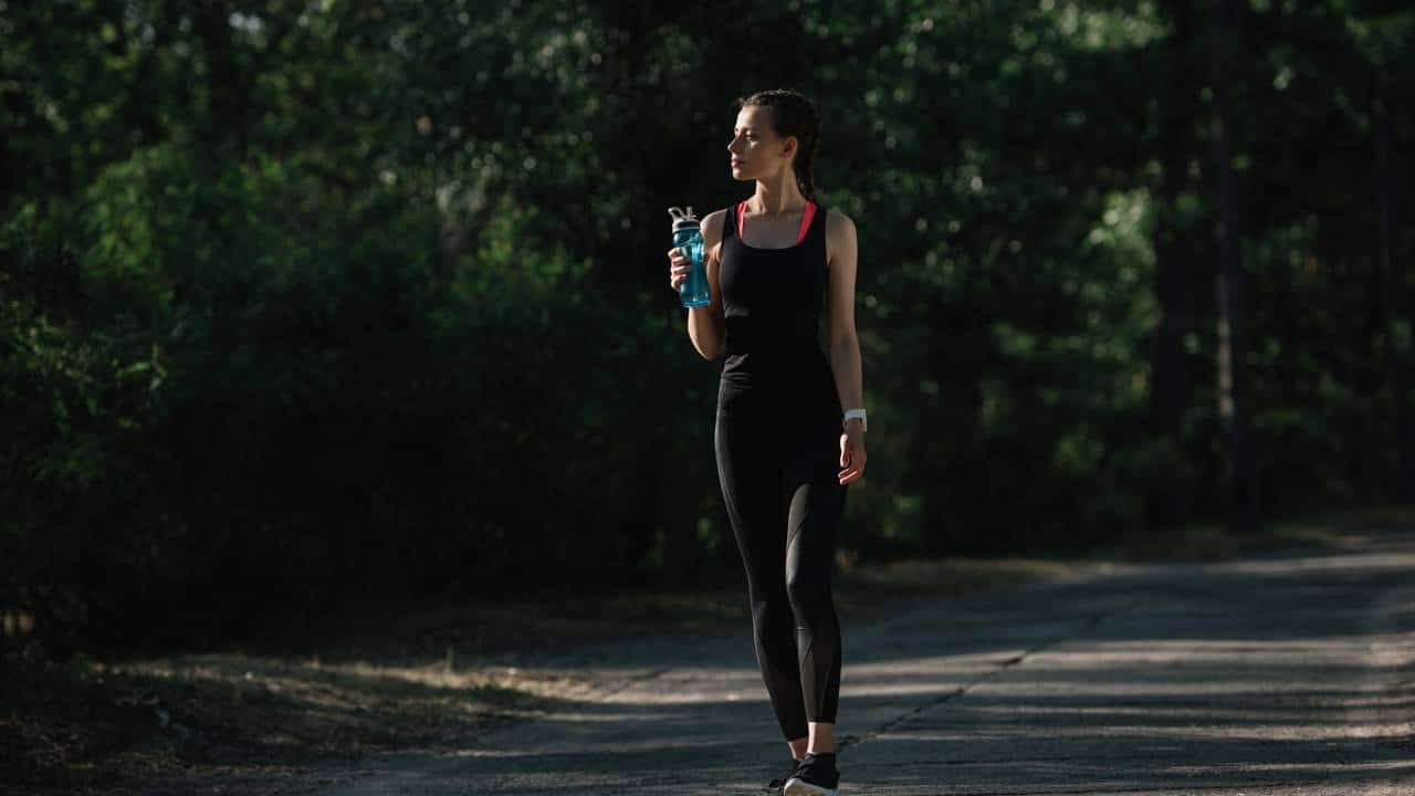 Mulher em trilha de caminhada se hidratando
