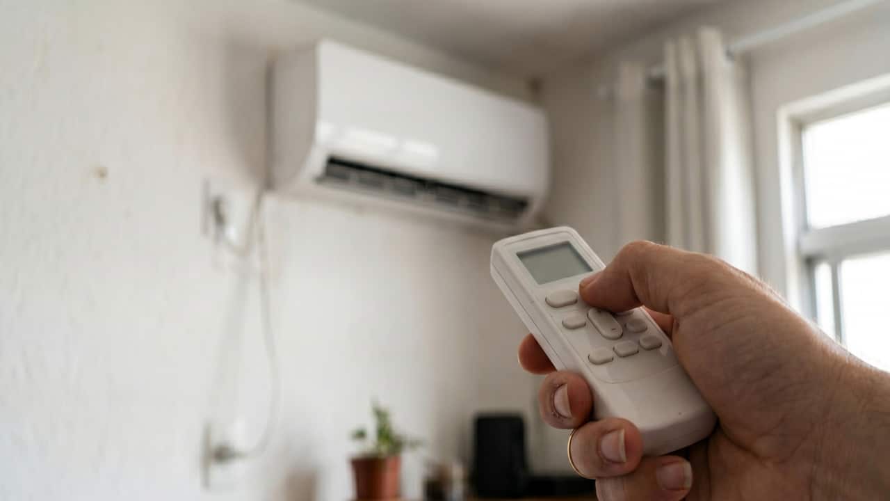 Pessoa com controle do ar condicionado em mãos para controlar a temperatura do aparelho