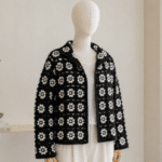 Manequim sem rosto usando cardigan de crochê preto com squares florais brancos, em ambiente minimalista e iluminado.
