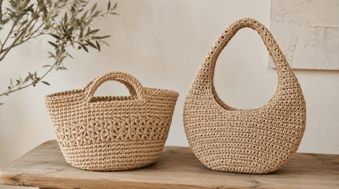 Duas bolsas de crochê em tom natural expostas lado a lado sobre uma bancada de madeira, em ambiente neutro e iluminado, destacando o acabamento artesanal e a textura rústica das peças.