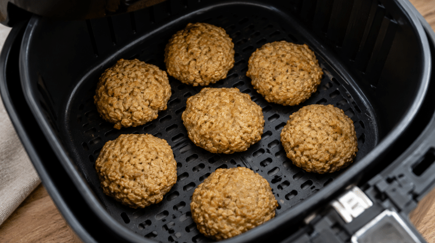 Bolinhos de banana com aveia assando dentro da cesta da Air Fryer, com aparência caseira, textura rústica e leve dourado.