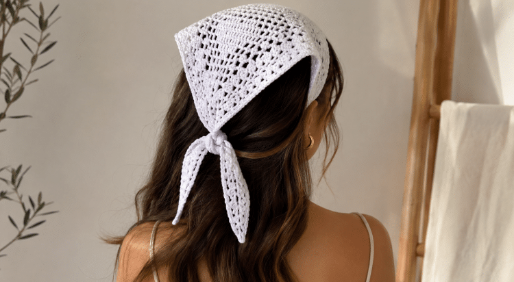 Mulher de costas usando bandana branca de crochê na cabeça, com cabelo castanho ondulado solto em ambiente interno claro e aconchegante.