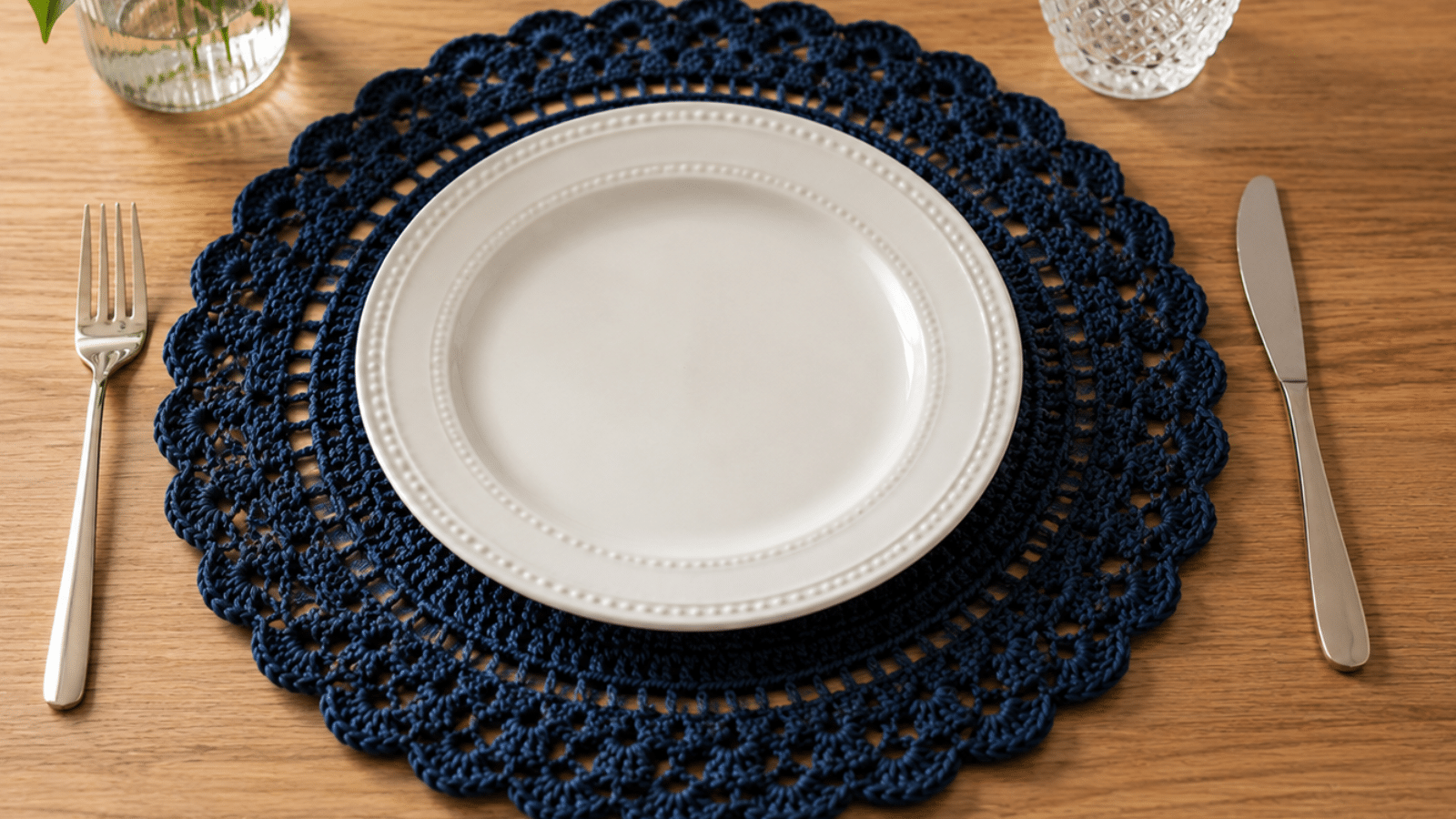 Sousplat de crochê azul-marinho em mesa posta simples, com prato branco e composição elegante em madeira.