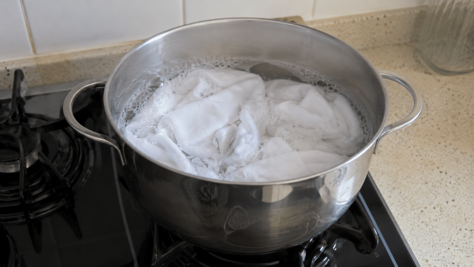 Panos de prato brancos dentro de uma panela com água quente e espuma